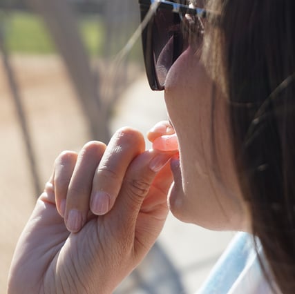 A woman wearing large black shades is taking a bite of a cannabis-infused edible.